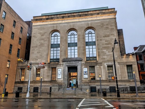 Historic building with large windows and decorative stonework, located on a rainy street corner.