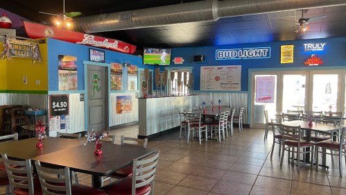Interior of a casual restaurant with tables, colorful walls, and a bar area displaying various beer signs.