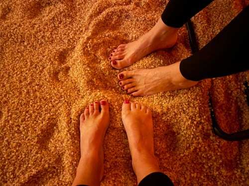 Two pairs of feet resting on a bed of salt, with one pair painted red and the other natural, in a warm, cozy setting.