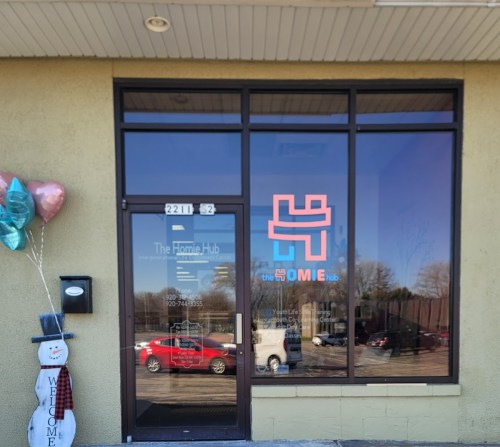 Exterior view of The Homie Hub storefront with a welcoming sign and festive decorations, including balloons and a snowman.
