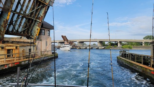 A view of a river with a raised bridge, fishing rods in the foreground, and a boat passing underneath.