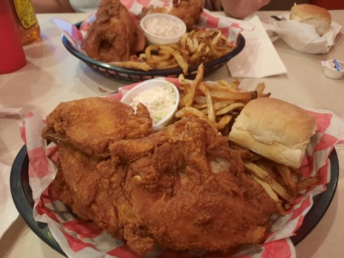 A basket of fried chicken, fries, a roll, and a small cup of dipping sauce on a table.
