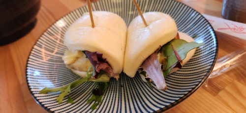 Two bao buns filled with greens, served on a patterned plate with toothpicks.