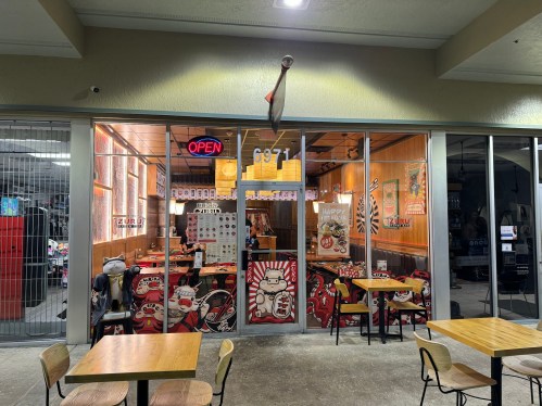 A restaurant storefront with an "Open" sign, featuring wooden decor and outdoor seating.