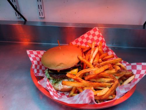 A burger with lettuce and cheese on a red checkered plate, accompanied by a generous serving of golden fries.