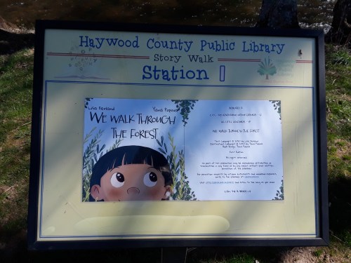 Sign for Haywood County Public Library's Story Walk, featuring the book "We Walk Through the Forest" at Station 1.