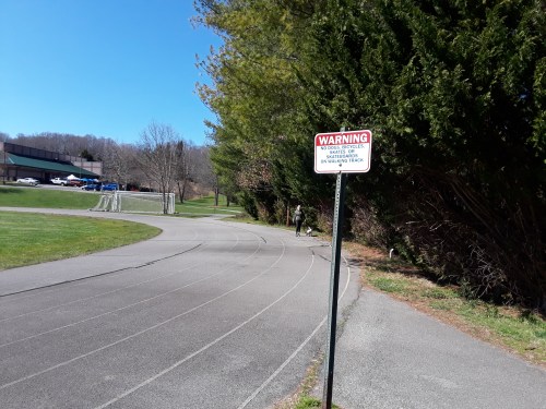 A winding track in a park with a warning sign and trees lining the path on a clear day.