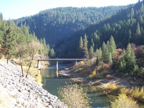 A serene landscape featuring a bridge over a river, surrounded by lush green mountains and trees.