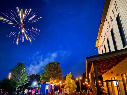 Fireworks illuminate the night sky above a building, with people gathered below enjoying the festive atmosphere.