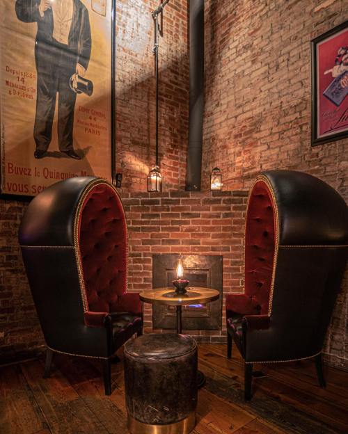 Cozy seating area with two high-backed chairs, a small table, and a warm glow from a candle near a brick fireplace.