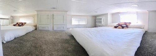 Cozy loft space with two beds, soft carpet, and natural light from windows. Decorated with colorful pillows.