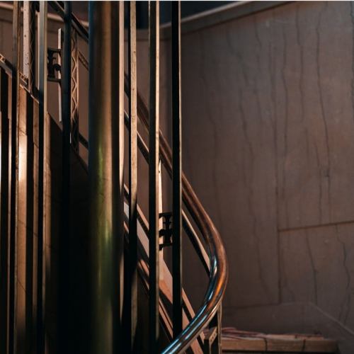A close-up of a curved staircase with metal railings and a textured wall in soft lighting.