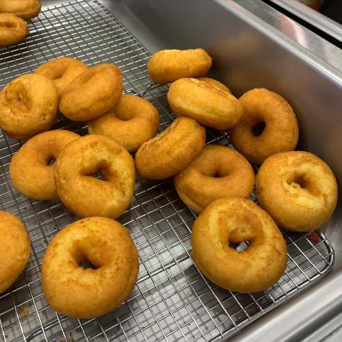 A tray of freshly fried, golden-brown donuts cooling on a wire rack.