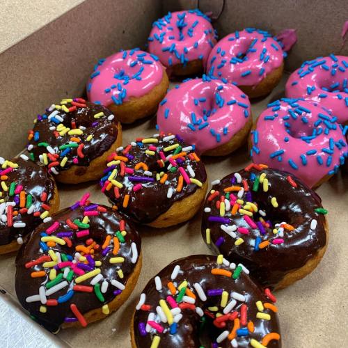 A box of assorted donuts: some with pink icing and sprinkles, others with chocolate icing and colorful sprinkles.