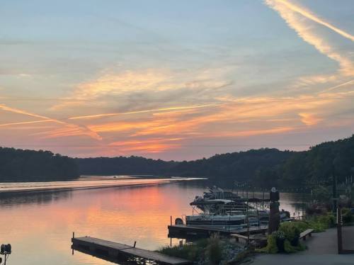 A serene sunset over a calm lake, with boats docked and colorful clouds reflecting on the water.