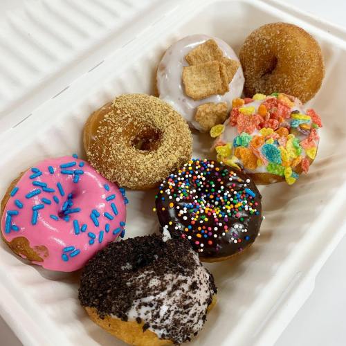 A variety of colorful donuts with sprinkles, frosting, and toppings in a takeout container.