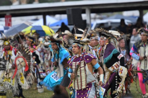 A group of Indigenous dancers in traditional attire perform at a cultural event, showcasing vibrant costumes and feathers.