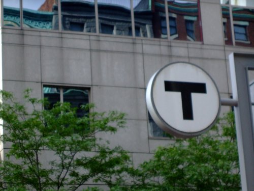 A circular sign with a large "T" in front of a modern building and green trees.