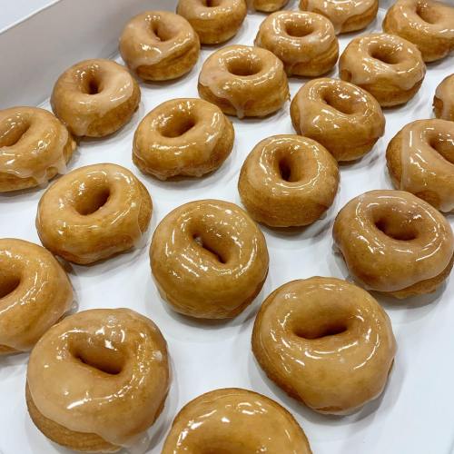 A box filled with glazed donuts arranged in neat rows, showcasing their shiny, golden-brown surface.