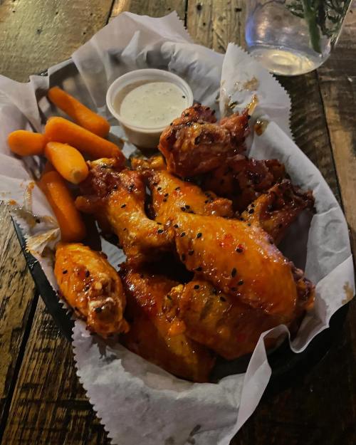 A basket of chicken wings with a side of carrots and ranch dressing on a wooden table.