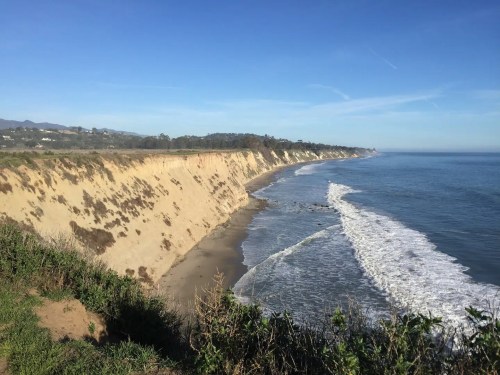 Coastal view of sandy cliffs and gentle waves under a clear blue sky.