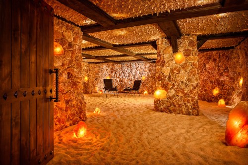 A serene salt cave with sandy floors, glowing salt lamps, and two chairs for relaxation. Warm, inviting atmosphere.