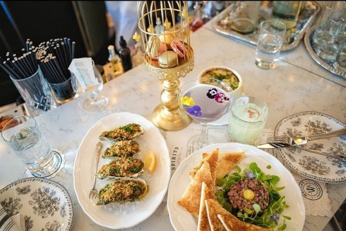 A beautifully arranged table featuring oysters, a salad, and a decorative dessert stand with macarons and flowers.