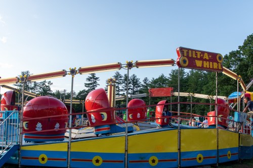 Colorful Tilt-A-Whirl ride at an amusement park, featuring red seats and a bright yellow base under a clear blue sky.