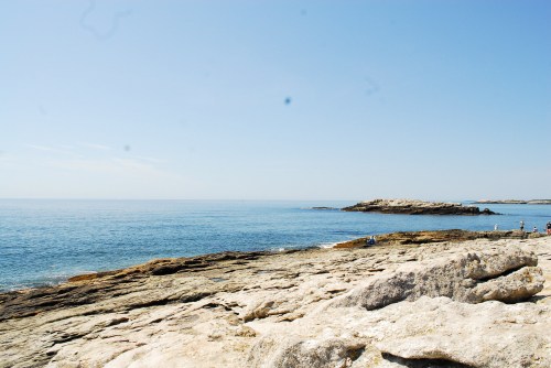 A serene coastal scene with rocky shores and calm blue waters under a clear sky.