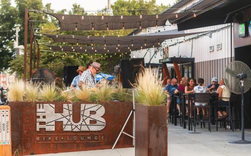A lively outdoor scene at The Hub Bike Lounge, featuring patrons enjoying drinks and live music under string lights.