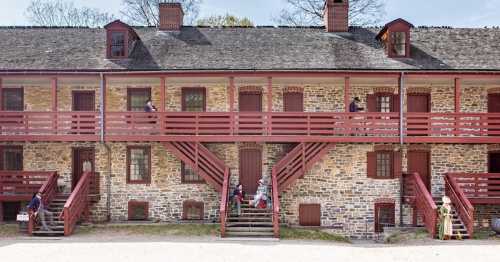 Historic stone building with red balconies, featuring people in period costumes on the stairs and walkway.