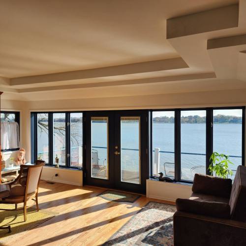 Bright living room with large windows overlooking a lake, featuring a chair, table, and a cozy sofa.
