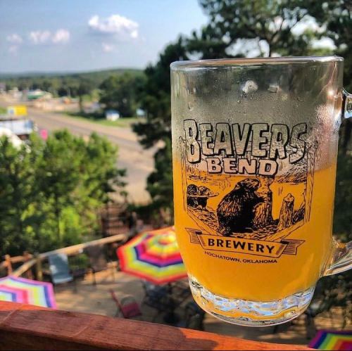 A frosty mug of beer with a scenic view of trees and colorful umbrellas in Hochatown, Oklahoma.