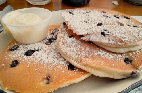 Three fluffy blueberry pancakes dusted with powdered sugar, served with a side of butter.