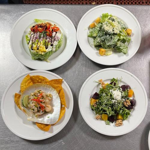 Four plates of colorful salads and tacos, featuring fresh greens, toppings, and a seafood taco on a scallop shell.
