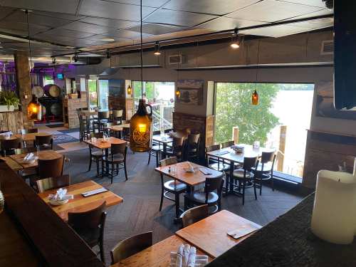 A cozy restaurant interior with wooden tables, chairs, and large windows overlooking a scenic view of water and trees.
