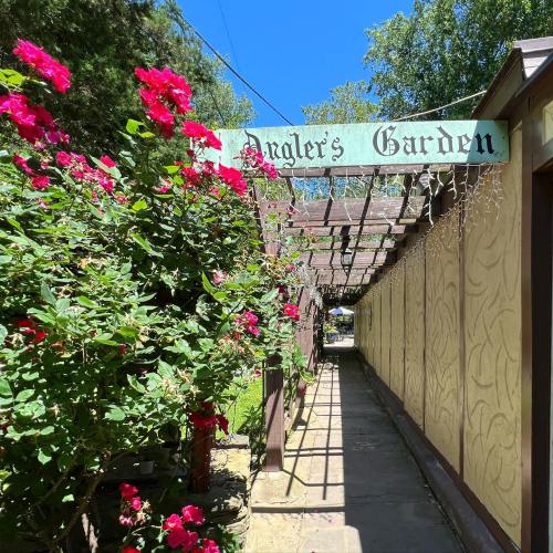 A pathway lined with pink flowers leads to a sign that reads "Angler's Garden" under a clear blue sky.