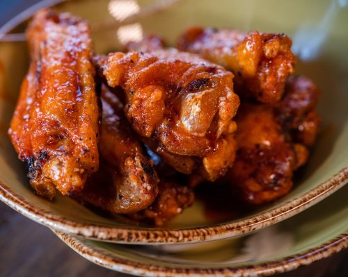 A close-up of crispy chicken wings coated in a spicy sauce, served in a decorative bowl.