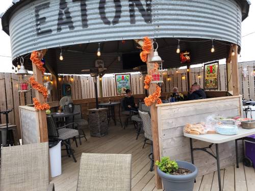 A cozy outdoor dining area with string lights, wooden walls, and tables, featuring people enjoying their meals.