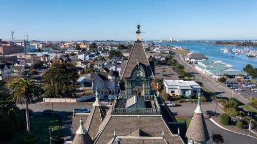 Aerial view of a coastal town featuring historic buildings, a clock tower, and a marina along the water.