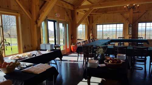 A spacious wooden room with tables set for dining, featuring a buffet and large windows overlooking a scenic view.