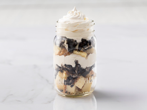 A mason jar filled with layers of cake pieces, whipped cream, and crushed cookies, topped with a swirl of whipped cream.
