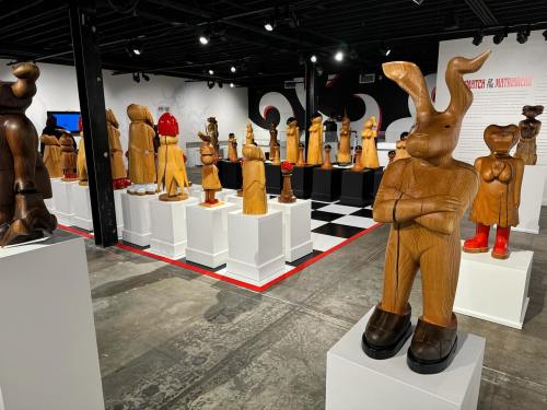 A gallery filled with wooden sculptures of various characters, displayed on pedestals in a modern art setting.