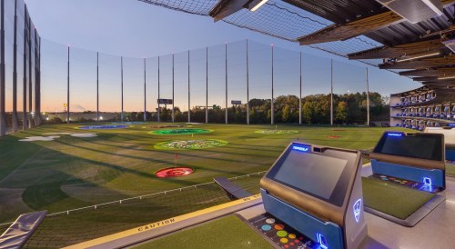 A panoramic view of a golf driving range at sunset, featuring colorful target areas and modern hitting bays.