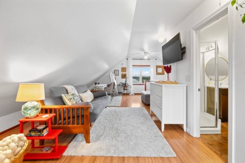 Cozy attic bedroom with a sofa, dresser, lamp, and bathroom access, featuring sloped ceilings and natural light.