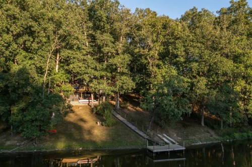 A serene lakeside view featuring a wooden dock, surrounded by lush green trees and a cozy cabin.