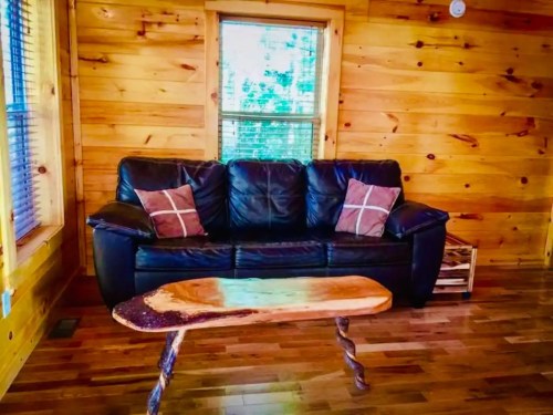 Cozy wooden cabin interior featuring a black leather sofa with pillows and a unique wooden coffee table.