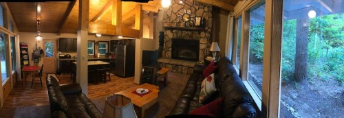 Cozy cabin interior with a stone fireplace, wooden beams, and a view of the forest through large windows.