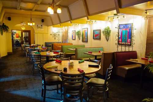 Cozy restaurant interior with colorful booths, tables set with napkins, and vibrant wall art. Warm lighting creates an inviting atmosphere.