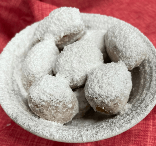 A bowl of powdered sugar-coated cookies arranged on a red cloth background.